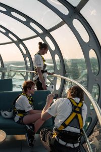 Abseil participants in a glass dome capture memories before starting their charity descent at sunset.