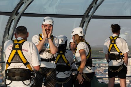 A nervous participant holds his face in anticipation, surrounded by fellow abseilers at a charity event.