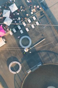 Aerial view of a charity abseil participant descending towards a rooftop event space at sunset.