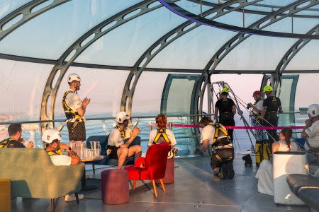 Participants and instructors inside a modern glass structure prepare for a charity abseil at sunset.