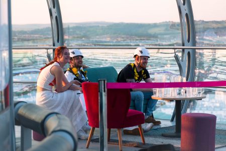 Three individuals in abseiling gear enjoying a relaxed moment with a scenic view before starting a charity abseil event.