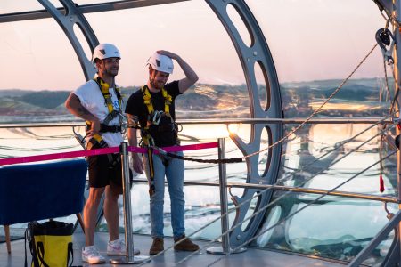 Two smiling participants in safety gear ready for a charity abseil event at dusk.