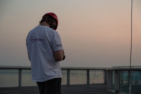 Photographer with red helmet reviewing images on camera with ocean background at dusk.