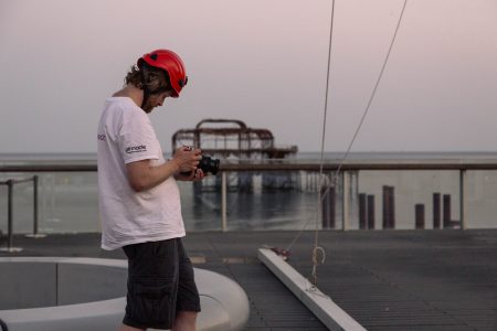 Photographer with red helmet reviewing images on camera with ocean background at dusk.