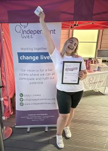 Joyful woman holding up a certificate and mug at Independent Lives charity event.