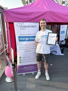 Young man with a certificate and mug in front of an Independent Lives event banner.