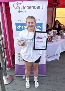 A proud participant holding a certificate and a mug in front of a banner for Independent Lives.