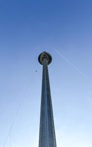 An adventurer abseiling down a tall, slender tower against a clear blue sky