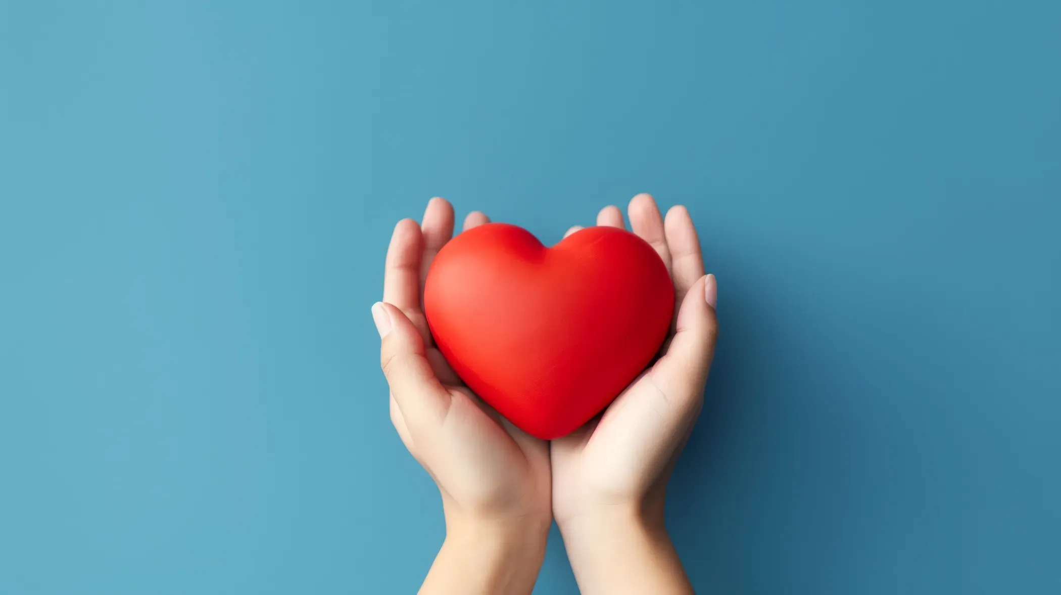 Two hands cradling a red heart against a blue background.