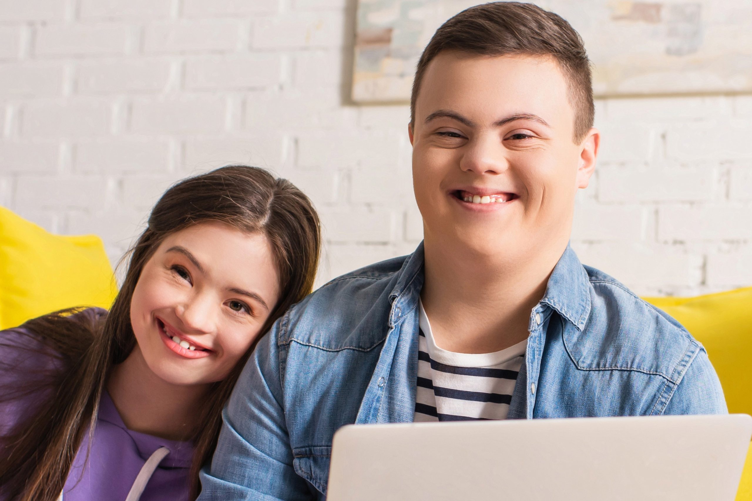 Young woman and man with Down syndrome smiling in front of a laptop