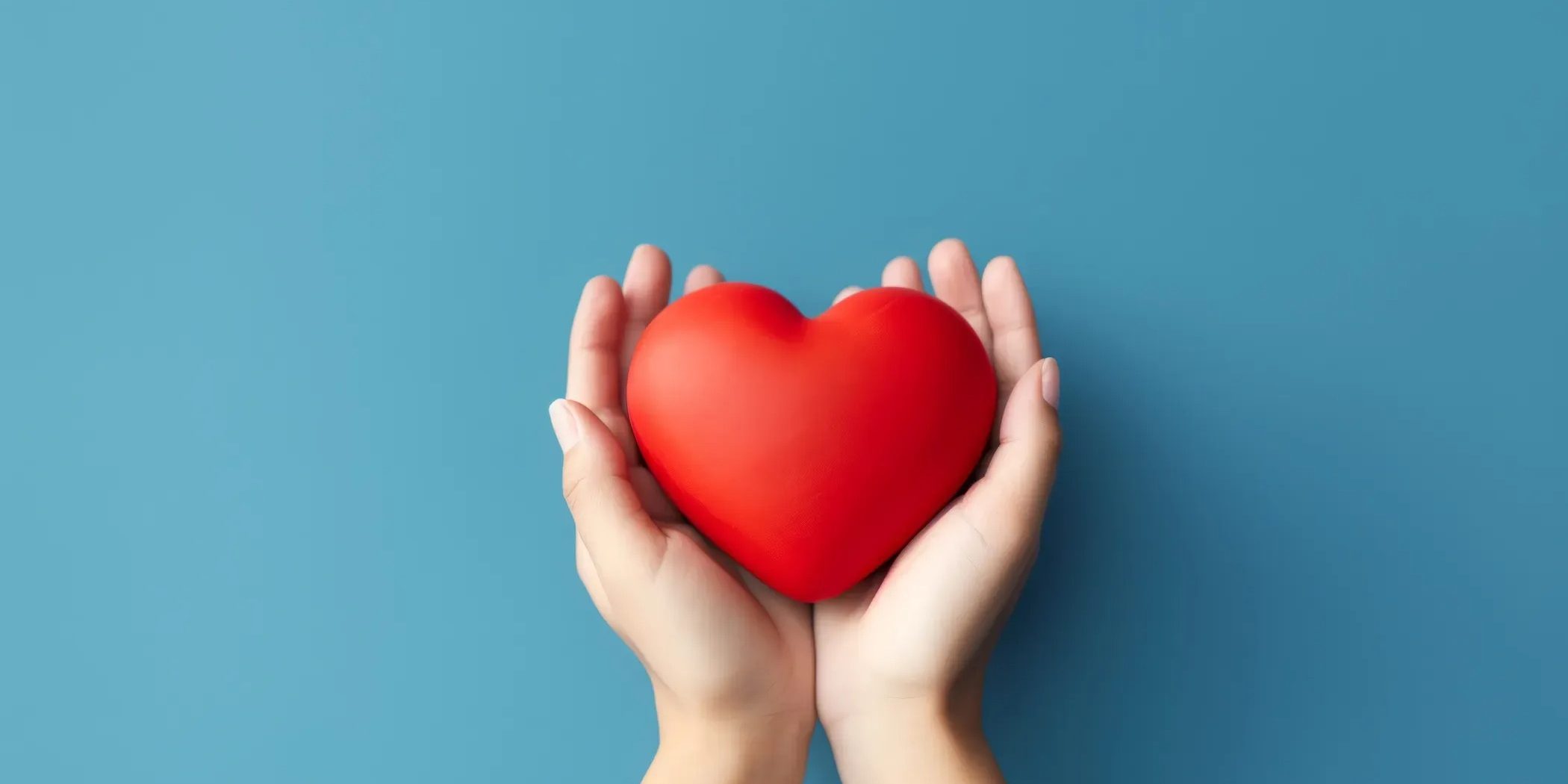 Two hands cradling a red heart against a blue background.