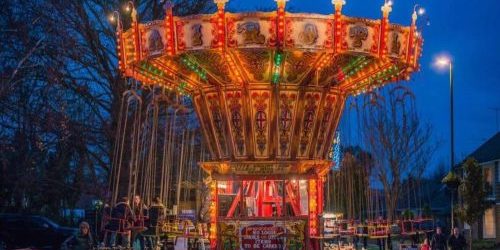 An illuminated vintage carousel at twilight with people nearby in a festive setting