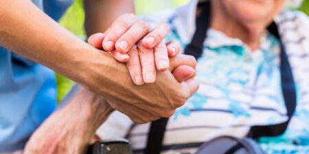 Caregiver holding elderly person's hand in a gesture of support.