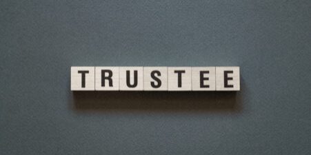 The word "TRUSTEE" spelt out in wooden letter blocks on a grey background.