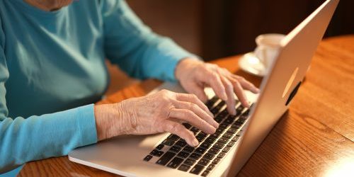 Extreme closeup of elderly womans hands while she types on laptop computer keyboard.