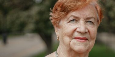 Elderly lady with red hair and a wise gaze in a park setting.