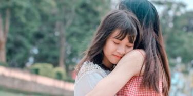 Young girl with a content smile embracing her mother in a park