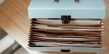 Opened teal accordion file organiser with multiple brown folders on a wooden desk.