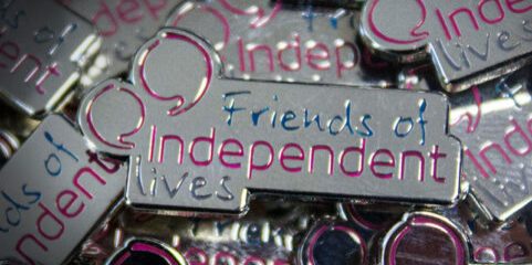 Close-up of "Friends of Independent Lives" pin badges with reflective silver and purple accents