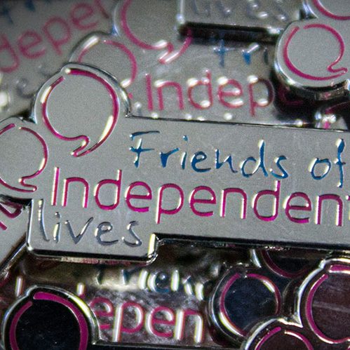 Close-up of "Friends of Independent Lives" pin badges with reflective silver and purple accents