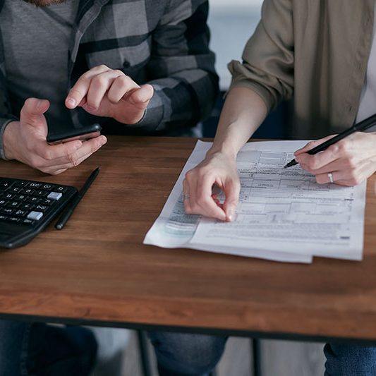 Two individuals engage in budget planning with a calculator and document on a wooden table.