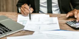 Professional working with documents and calculator at a wooden desk.