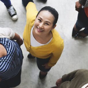 A diverse group of individuals forming a circle and looking down towards the camera with smiles.