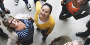 A diverse group of individuals forming a circle and looking down towards the camera with smiles.