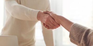 Two people holding hands in a show of support and trust, backlit by a warm indoor light.