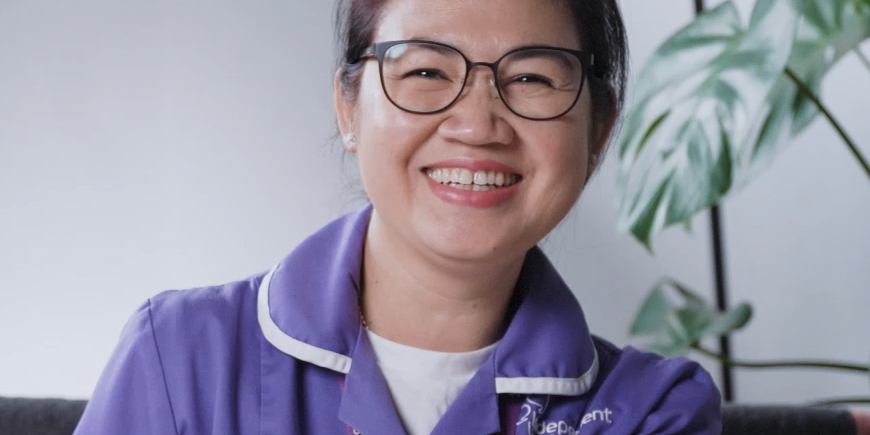 Smiling healthcare worker in purple uniform with staff lanyard