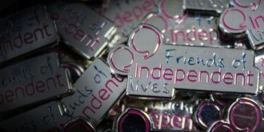 Close-up of "Friends of Independent Lives" pin badges with reflective silver and purple accents